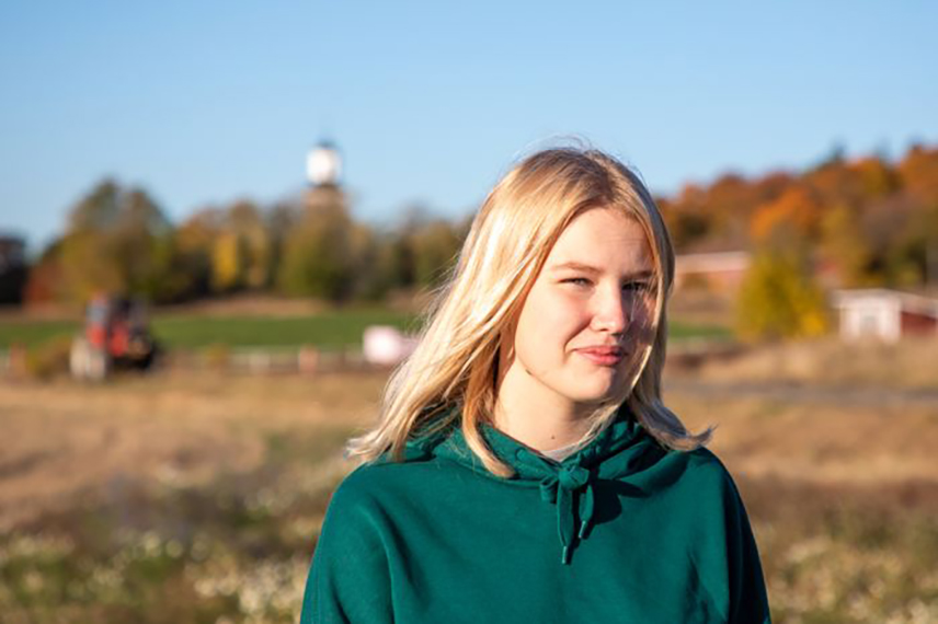 Fotografi på Thelma med vind i håret och jordbrukslandskap i bakgrunden